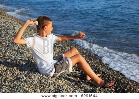 Siddende dreng kaster sten i havet