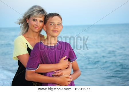 Ung kvinde omfavner smilende dreng på stranden i aften