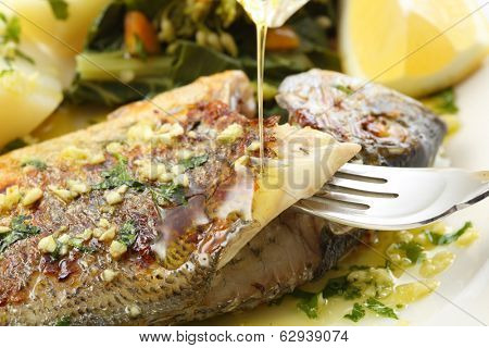 pouring olive oil on very fresh seabream fish grilled - traditional food from Portugal