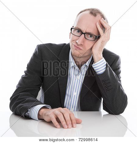 Frustrated businessman wearing glasses sitting at desk with head in hand isolated on white background