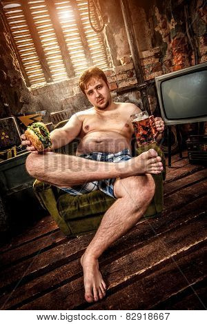 Fat man eating a hamburger sitting on a chair in the slums