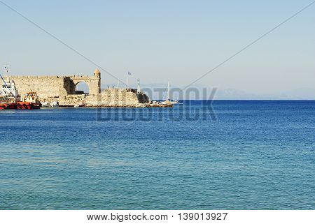 fortress with lighthouse and flag at the harbor in Rhodes