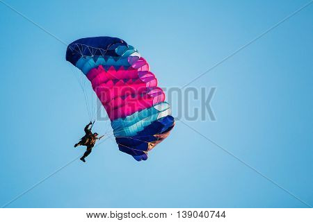 Skydiver On Colorful Parachute In Blue Clear Sky. Active Lifestyle Extreme Hobbies