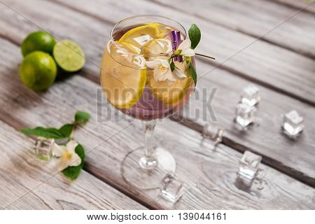 Ice and lemon inside beverage. Sliced fruit and small flower. Tom collins with expensive gin. Juice mixed with cold water.
