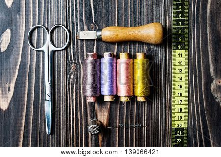 Accessories for sewing on dark wooden table - seam ripper, thread, scissors, centimeter, measuring tape.