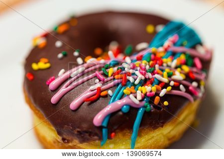 A close up of a doughnut with chocolate icing colorful sprinkles and drizzled blue and pink icing.
