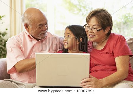 祖父母と自宅でラップトップ コンピューターを使用しての Grandaughter