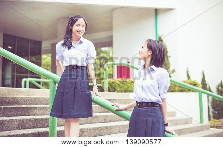 Cute Asian Thai high schoolgirls student couple in school uniform stand on the stairway making eye contact in vintage childhood color