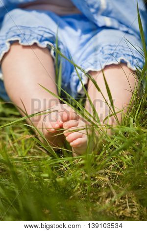 Feet of a small baby on the green grass. Sunny day. Cute child sitting on the ground. Barefoot of a infant.