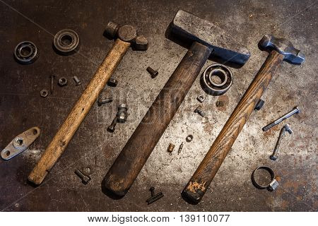 Three old steel hammers with wooden handles and some bolts nuts bearings valves washers nails on the metal background