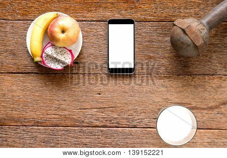 Smart phoneIron dumbbell and milk with fruit (bananaappkedragon fruit) on wooden floor.Top view focus.