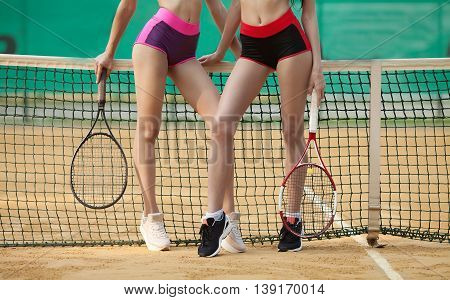 Two sexy slim fitness woman long legs in sports clothing holding tennis racket on clay court