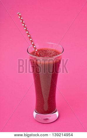 closeup of a red detox smoothie served in a glass jar with a red drinking straw patterned with white dots, on a pink background