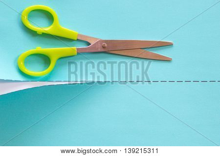 A green scissors cutting in blue paper