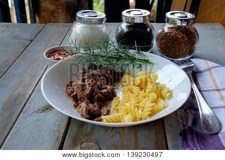 Plate with stewed meat and spiral pasta on rustic wooden table