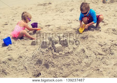 little boy and girl building sand castle on summer beach