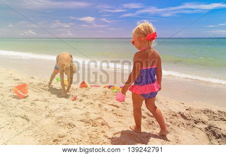 little boy and girl play with sand on summer beach
