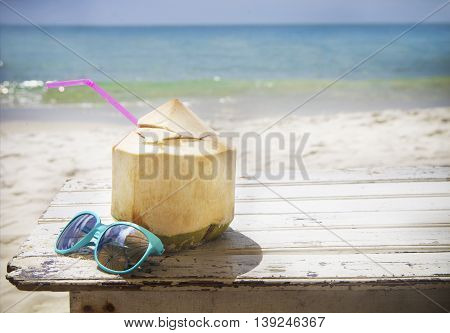 Fresh coconut cocktail and blue sunglasses on tropical beach
