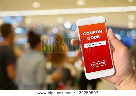 Woman hand holding smartphone against blur bokeh of mall background with word coupon code buy now