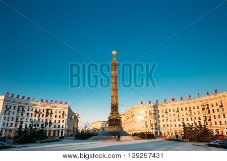 Minsk, Belarus - March 10, 2015: Monument With Eternal Flame In Honor Of The Victory Of The Soviet Army Soldiers And Partisans Of Belarus In The Great Patriotic War. Victory Square In Minsk - Symbol Belarusian Capital. The Inscription On The Building - fe