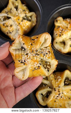 bun puff pastry with spinach and ricotta in a hand on a background of trays baking