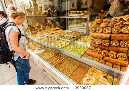 Showcase with Oriental sweets with nuts in assortment. Tourist female standing and looking in the window with oriental sweets on the streets of Istanbul. Shop with sweets. Travel Turkey.