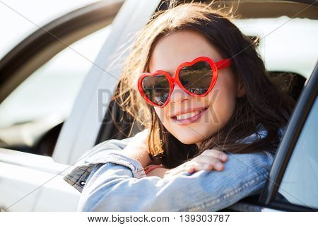 summer holidays, valentines day, travel, road trip and people concept - happy teenage girl or young woman heart shaped sunglasses in car