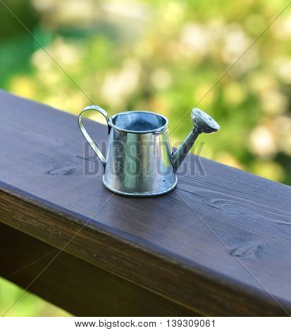 Close up of cute small watering can on wooden planks in the garden. Summer seasonal background, rural countryside still life, vintage or retro concept
