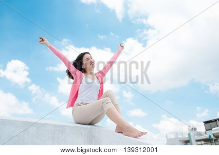 Freedom concept. Enjoyment. Asian young woman relaxing under blue sky on rooftop with her hands raised towards sky