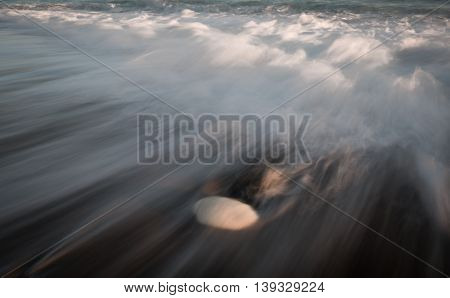 Sea waves crashing into the shore and flowing above a white pebble. Long exposure photography