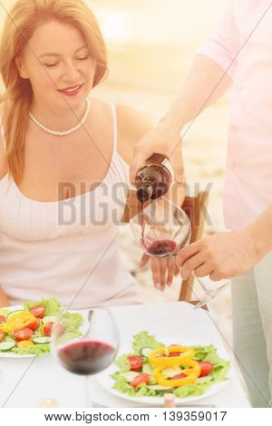 Toned picture of professional sommelier demonstrating red wine to beautiful woman. Red-haired woman looking at sommelier pouring red wine in her glass.