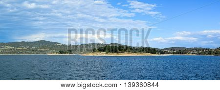 Lake Jindabyne landscape with a blue sky and some clouds.  The lakes two largest islands are pictured in the centre -  'Lion Island' (right) and 'Cub Island' (left).  Jindabyne township can be seen to the right of Lion Island.