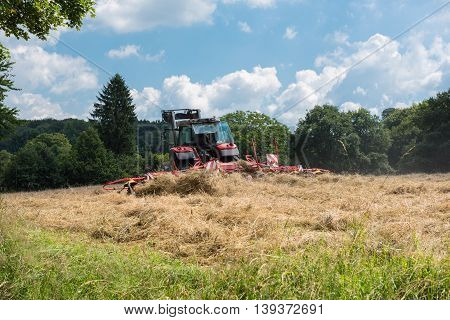 tractor with tedder turning hay on the meadow