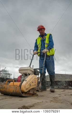 Tobolsk, Russia - July 15. 2016: Sibur company. Construction of plant on processing of hydrocarbonic raw materials. Builder worker at sand ground compaction with vibration plate compactor machine