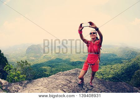 young woman hiker use smartphone taking self photo on seaside mountain top