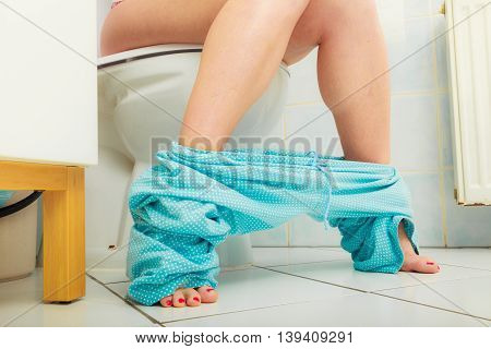 Woman with constipation or diarrhoea sitting on toilet with her blue pajamas down around her legs