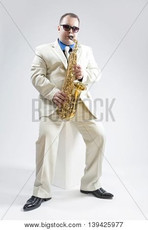 Music Concepts and Ideas. Portrait of Hadnsome Male Saxophone Player Performing In Studio Environment. Wearing White Suit and Sunglasses. Vertical Composition