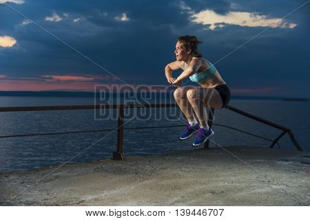 Young caucasian woman in sportswear doing plyometric exercises on pier. Fitness workout outdoors