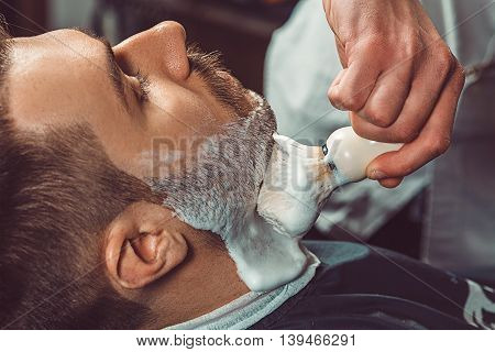 Hipster client visiting barber shop. The hands of young barber making the cut of beard