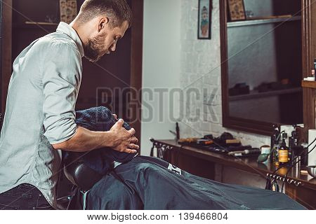 Hipster client visiting barber shop. The hands of young barber making the cut of beard