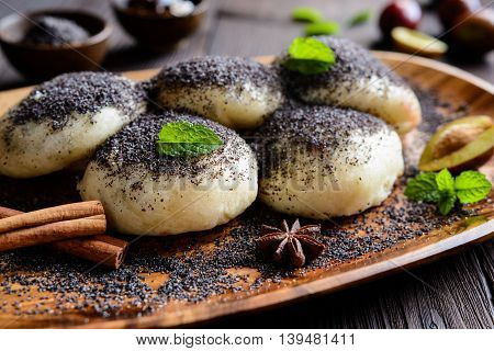 Traditional sweet steamed dumplings with a plum jam, sprinkled with ground poppy seeds on a wooden plate and background