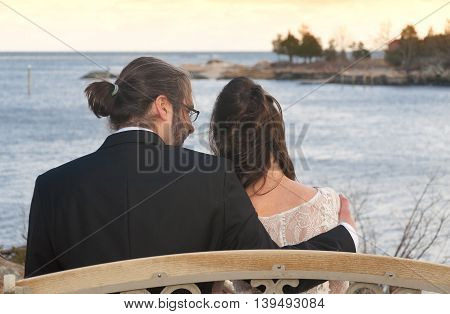 a bride and groom sitting on a bench outside overlooking Long Island Sound in Branford Connecticut.