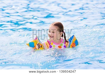 Happy laughing little girl playing in outdoor swimming pool on a hot summer day. Kids learn to swim with colorful floaties.