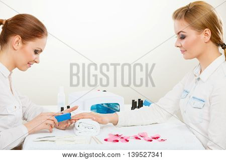 Relaxing time and wellness day concept. Blonde elegant woman visiting professional manicurist salon. Beautician makes perfect nails to client.