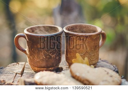 Two Clay Rural Cup with Hot Beverage are on the Wooden Stumb with Autumnal Leaves.Nature Background.Selective Focus.Toned