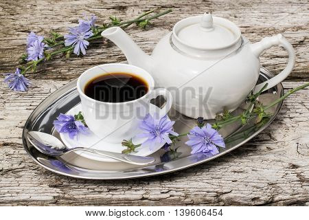 Medicinal plant chicory. The roots of the plants are used as a substitute for coffee. Drink from chicory in a cup and teapot on a metal tray on the old wooden background. Rustic style