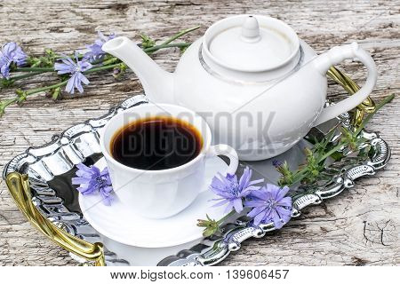 Medicinal plant chicory. The roots of the plants are used as a substitute for coffee. Drink from chicory in a cup and teapot on a metal tray on the old wooden background