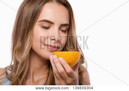Magnificent fruit. Pleasant delighted woman holding orange and smelling it while standing isolated on white background