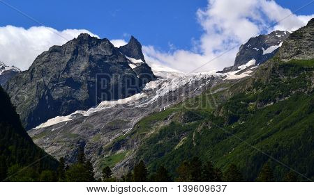 Mountain peaks and snow on a background of blue sky and clouds. Dombay - a mountainous area in Karachay-Cherkessia in the basin of the Teberda in the North Caucasus (Russia). Photo taken on: July 26 Friday 2013