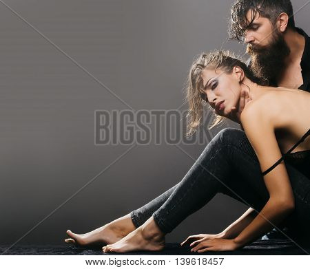 young couple of pretty sexy woman in black jeans and bra has slim body and handsome bearded man with long beard in shirt on grey background copy space
